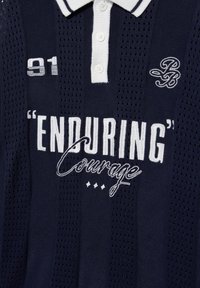 Polo bleu marine avec des boutons blancs, « ENDURING » et « Courage » brodés en blanc, avec les logos « 91 » et « LB » stylisés sur la poitrine.