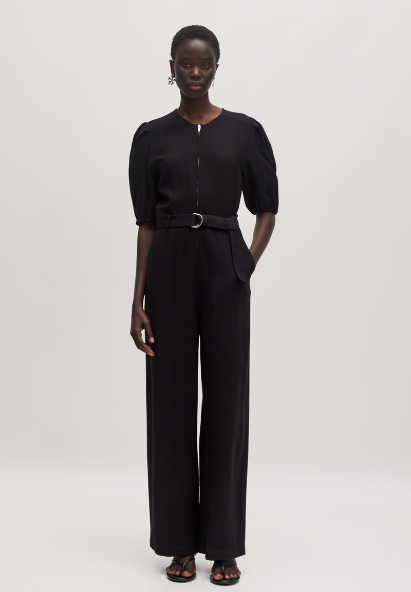 Zwarte jumpsuit met korte pofmouwen, rits aan de voorkant en riem in de taille. Heeft brede pijpen en subtiele zakdetails. Gladde fabric textuur.