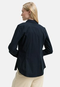 Navy blue shirt, lightweight fabric, tailored fit with a slightly structured collar. Features back darts and a curved hem. No visible hardware.