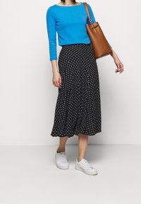 Blåtröja, knälång svart kjol med vita prickar, och vita sneakers. En brun axelväska bärs på höger arm.