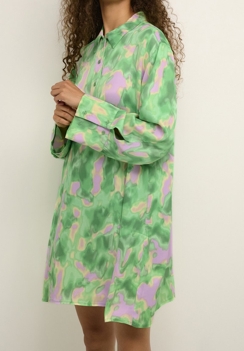 Langärmliges Shirtkleid in grünen, pinken und lavendelfarbenen abstrakten Mustern; glattes Material mit Kragen und Knopfverschluss, endet oberhalb des Knies.