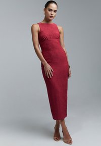 Ribbed, tiukasti istuva midi-mekko syvässä punaisessa, pyöreällä pääntiellä ja hienovaraisella kokoamisella vyötäröllä. Sujuva tekstuuri ja tyylikäs siluetti.