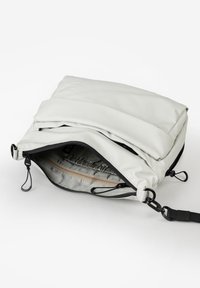 Borsa a tracolla in morbido tessuto grigio chiaro con zip nera, aperta che mostra la tasca interna con zip e la tracolla nera regolabile con ganci a clip.