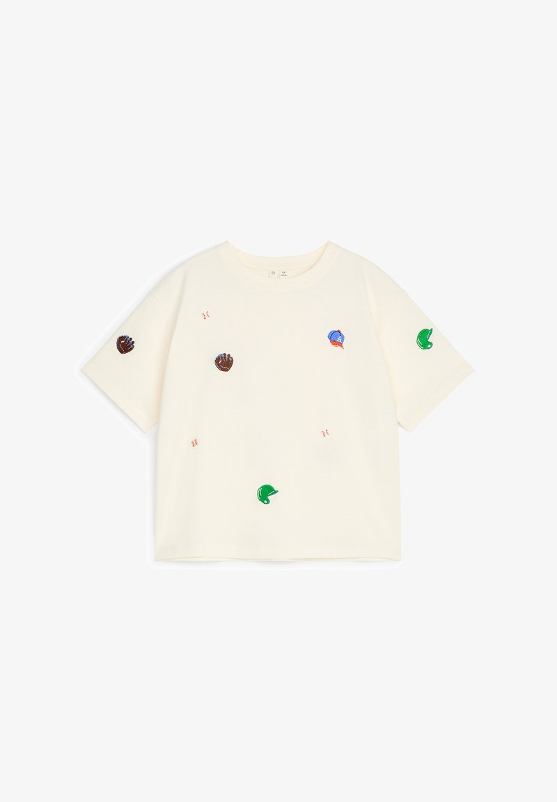 Chemise à manches courtes couleur crème avec de petits gants de baseball, casques et balles de baseball brodés disséminés sur le devant et les manches.