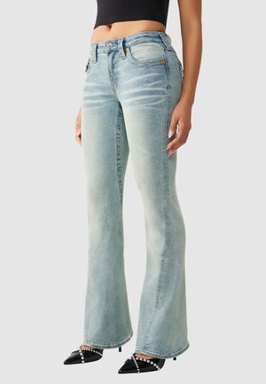 Jean flare bleu clair délavé porté avec des talons noirs à bout pointu ornés de perles et un crop top noir.