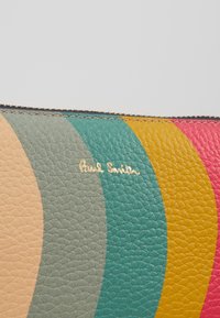 Article en cuir avec des rayures courbes crème, gris, vert, jaune et rouge, avec un petit texte doré "Paul Smith" et un bord de fermeture éclair visible.