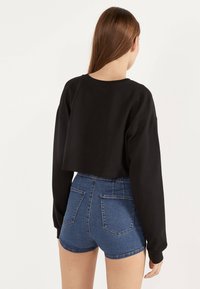 Mustat lyhyt cropattu collegepaita pitkillä hihoilla, yhdistettynä korkeavyötäröisiin sinisiin farkkushortseihin, joissa on kaksi takataskua ja kapea malli.