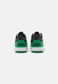 Grønne og svarte sneakers med hvit såle. Har en teksturert overflate og en løftestropp, med "PUMA"-logoen tydelig vist på hælen.