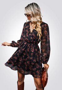 Vestido negro floral hecho de tela transparente; cuenta con mangas largas, un escote en v y una cintura fruncida. Patrones de flores en rojo oscuro y rosa por todo el diseño.