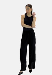 Zwarte mouwloze top met ronde hals, gecombineerd met hooggetailleerde, geplooide zwarte wijde broek. Glanzende zwarte puntige schoenen maken de look af.