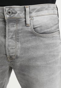 Grå denimjeans med en klassisk passform, som har en framficka, förstärkt sömnad och en metallknappstängning. Subtil blekning för struktur.
