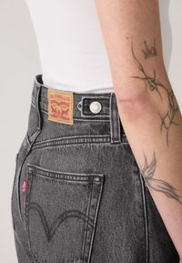 Hoge taille, zwarte denim jeans met een label waarop "Levi Strauss & Co." staat en zichtbare stiksels; heeft een klassiek ontwerp van de achterzak.