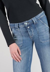 Light blue denim jeans with a high waist, two buttons, and front pockets. The fabric has a faded texture with visible stitching details.