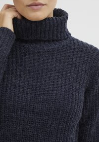 Knitted navy sweater with a high, textured turtleneck. The fabric features a ribbed pattern and a cozy, thick appearance.