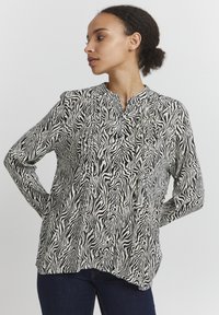 Blusa a maniche lunghe a stampa zebra in bianco e nero con colletto alla mandarino, caratterizzata da dettagli plissettati e una vestibilità comoda.