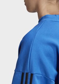 Sweat-shirt bleu à col rond, orné de trois bandes noires sur l'épaule, fabriqué dans un tissu lisse et extensible.