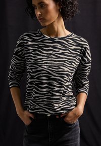 Pull à rayures noir et blanc avec une coupe ample, col rond et manches trois-quarts, associé à un jean foncé.