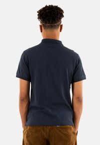 Mörkblå pikétröja med korta ärmar, strukturerad tyg och klassisk krage. Har en liten märkesetikett på fållen.