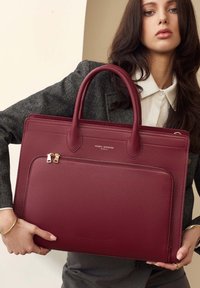 Burgundy leather tote with dual handles, zip closure, and one front pocket. Features gold-tone hardware and textured finish.