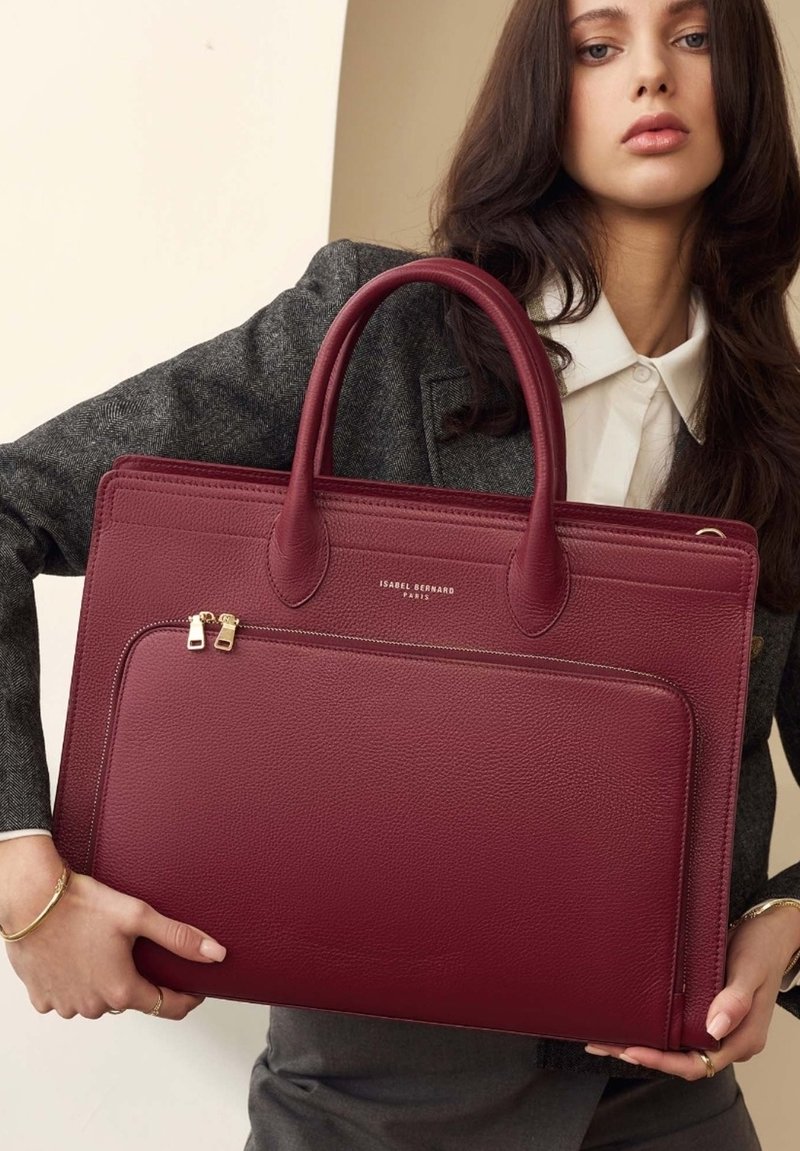 Burgundy leather tote with dual handles, zip closure, and one front pocket. Features gold-tone hardware and textured finish.