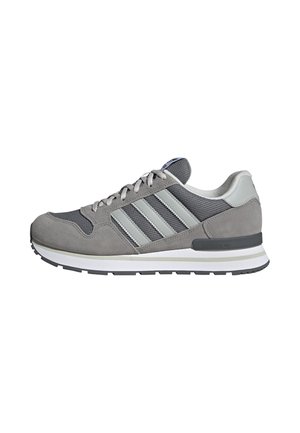 Szaro-białe buty sportowe Adidas z materiałami mesh i zamszowymi, z przodu sznurowane i z charakterystycznymi trzema paskami z boku.