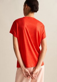 Rød kortærmet t-shirt, letvægtsstof, afslappet pasform, rund hals, med subtil tekstur og dekorativ syning langs skuldrene.