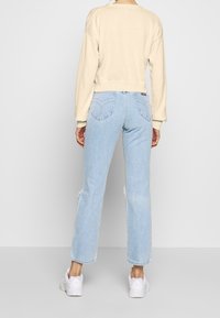 Krämfärgad kort tröja, ljusblå högmidjade jeans med hjärtformad stickning på fickorna, kombinerat med vita sneakers.