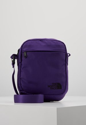 Small purple shoulder bag with a front zipper pocket and adjustable strap, branded with The North Face logo on the lower right corner.