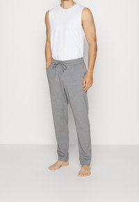 Šedé bavlněné tepláky s elastickým pasem, stahovací šňůrkou, bočními kapsami a zúženým střihem nohavic, v kombinaci s bílým tílkem.