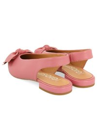 Zapatos de piel rosa tipo slip-on con detalle de lazo, lados abiertos y suela de goma plana y texturizada. Presentan una plantilla en contraste color marrón con la marca.