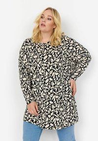 Tunic nera con un motivo geometrico crema, maniche lunghe, scollatura rotonda e vestibilità comoda, abbinata a jeans azzurri chiari.