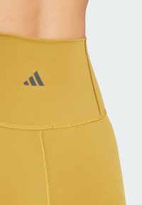 Leggings jaunes taille haute en tissu extensible. Présentent des coutures à plat et un petit logo noir près de la taille.