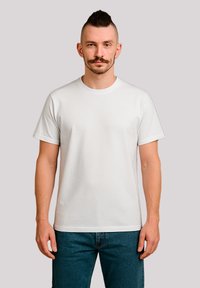 Weißes Baumwoll-T-Shirt mit kurzen Ärmeln und Rundhalsausschnitt, figurbetontes Design, vor einem neutralen Hintergrund präsentiert, kombiniert mit blauen Jeans.