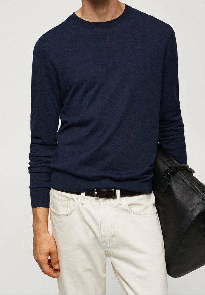 Pull tricot bleu marine à col rond et manches longues, associé à un pantalon couleur crème et un sac en cuir noir.