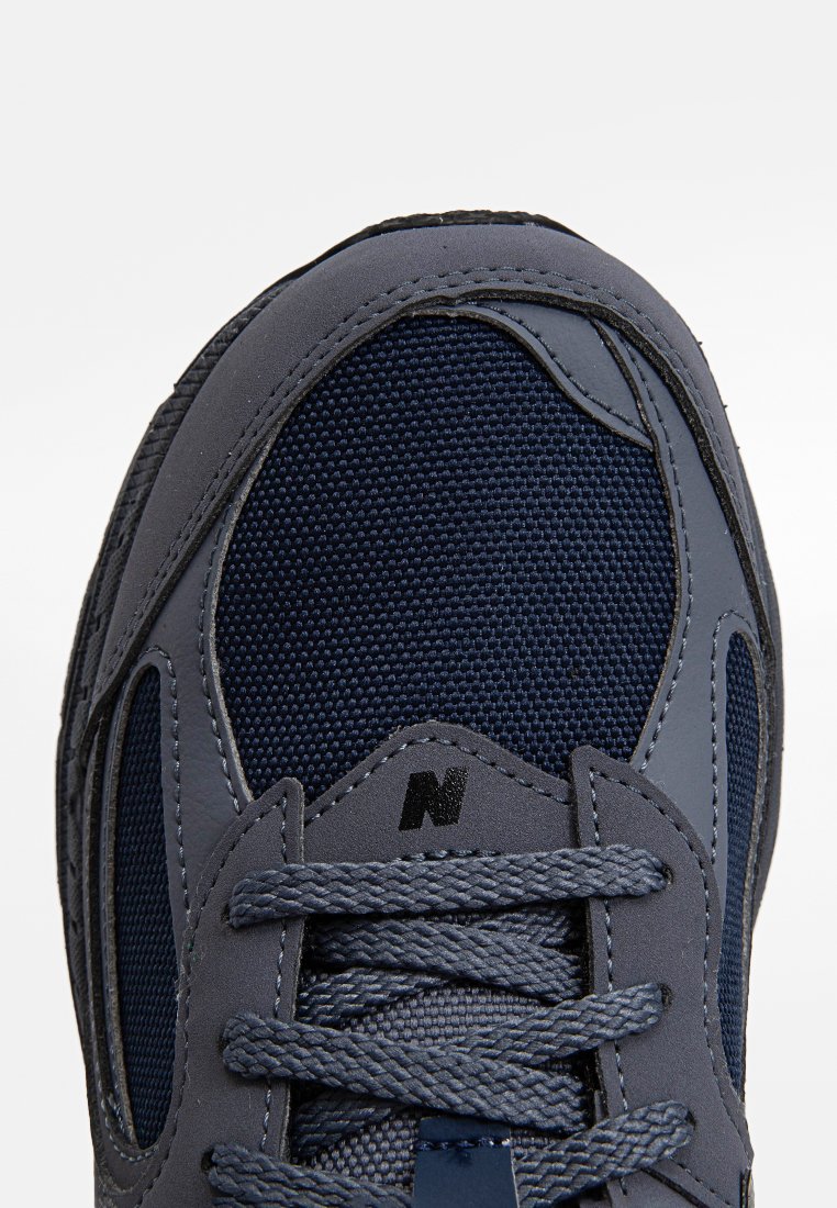Marineblaue Sneaker mit einer strukturierten Mesh-Oberfläche, glatten synthetischen Überzügen, dicken Schnürsenkeln und einem auffälligen 'N'-Logo an der Seite.