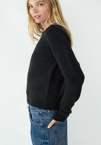 Zwarte gebreide trui met lange mouwen, ronde hals en een losse pasvorm, gecombineerd met versleten blauwe denim jeans. Zachte textuur.