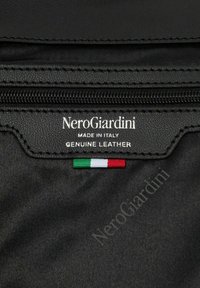 Sort læderprodukt med lynlås, der har "NeroGiardini" mærkning, "Made in Italy" og en lille italiensk flag detalje.