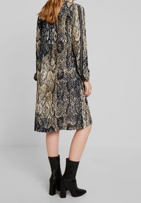 Dlouhé šaty s hadím potiskem v odstínech černé, béžové a hnědé; mají volný střih a zaoblený lem. Kombinováno s černými kotníkými botami.