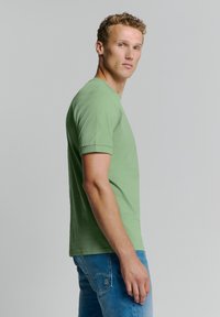 Lichtgroen T-shirt met korte mouwen van katoen. Heeft een ronde halslijn en een relaxte pasvorm, gedragen met blauwe denim jeans.