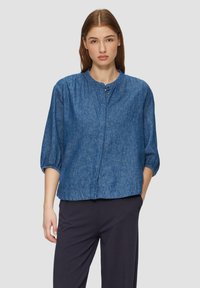 Blauwe denimshirt met een ronde hals, driekwartmouwen en twee knopen aan de voorkant. Heeft een relaxte pasvorm en een zachte textuur.
