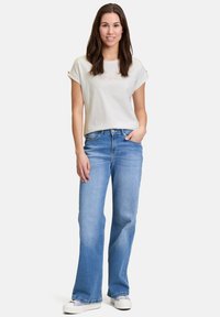 Lys grå kortærmet t-shirt med pink grafik, parret med lyseblå flare jeans og hvide sneakers, hvilket skaber et afslappet outfit.