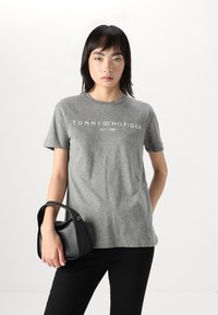 Šedé bavlněné tričko s krátkými rukávy, s potiskem "TOMMY HILFIGER EST. 1985" v bílé barvě. Doplněno malou černou kabelkou.