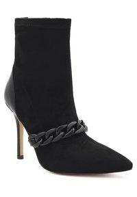 Stivale alla caviglia in suede nero con punta affusolata, caratterizzato da un elegante dettaglio a catena nera lucida attorno alla caviglia e un alto tacco a stiletto.