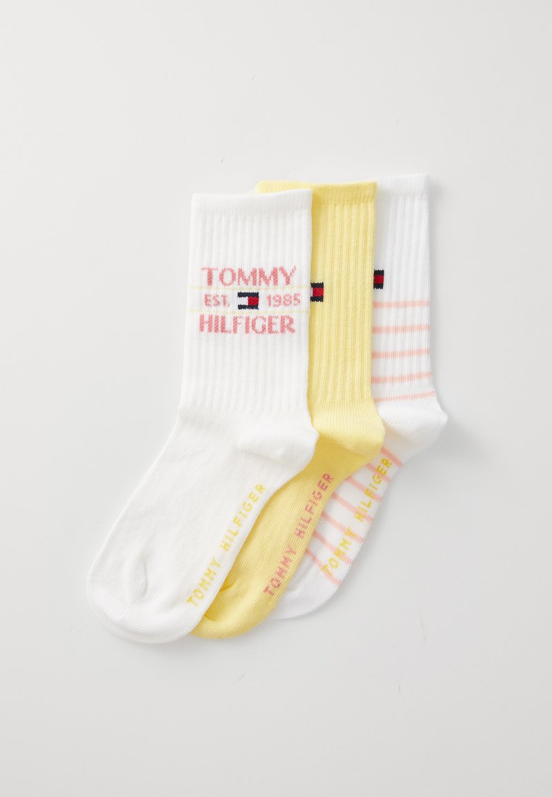 Tre par ribbede bomullssokker: en hvit med rosa tekst, en gul med minimal design, og en hvit med rosa striper.