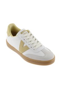 Vita och beige avslappnade sneakers med tan gummisula, vita snören och beige "V"-logotyp på sidan, vinklad för att visa ytter- och ovansidan.