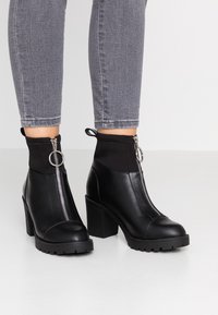 Schwarze Knöchelstiefel mit einem kräftigen Absatz und Reißverschluss. Aus Leder mit einem elastischen oberen Bereich. Strukturierte Sohle für besseren Halt.