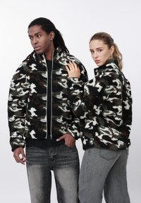 Bløde, lynlåslukkede jakker i sort, hvid og brun camouflagemønster med høje kraver og blød tekstur; båret af to modeller.