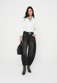 Άσπρο υπερμεγέθες πουκάμισο με φαρδιά μανίκια, γκρι τζιν, μαύρη ζώνη με αγκράφα σε σχήμα καρδιάς, μαύρη τσάντα χειρός και καφέ μυτερές μποτάκια μέχρι τον αστράγαλο.