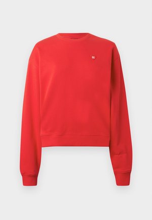 Sarkanais kokvilnas džemperis ar garām piedurknēm, noapaļotu kakla izgriezumu un ribotu malu. Krūtīs ir neliels balts logo. Gluda tekstūra.