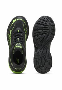 Zapatos deportivos negros con acentos en verde neón, parte superior de malla, cuello acolchado y suela de goma texturizada con surcos multidireccionales.